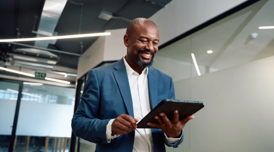 African business professional holding a tablet in a modern office with glass walls.