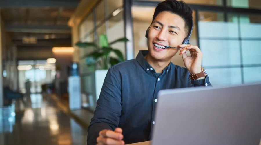 Smiling young Asian professional wearing a headset in a work setting.
